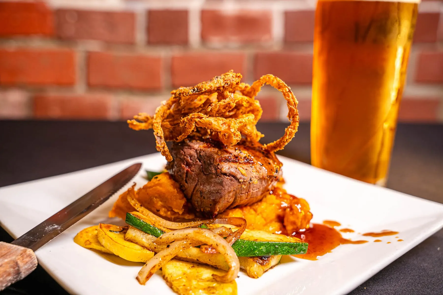 Steak with mashed potatoes, grilled vegetables, fried onions and a beer